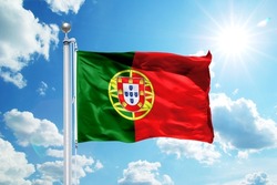 National Portugal flag waving in the wind, against the blue sky. Wavy flag in the sky with sunbeams.