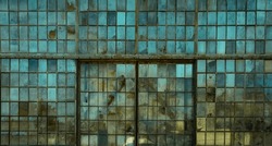 Broken windows on an old abandoned industrial factory building, framed by rusty metal and smudged by dirty glass. A widescreen image with the blue sky reflecting in the panes.