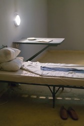 Photo of the interior of the prison. bed and desk with lamp.