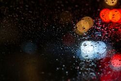 Drops of Rain Water In Night or Evening Street Lights on car Glass Background. Street Bokeh Lights Out of Focus. Water drop on window. Out of focus, Bokeh light. Tailights and traffic in bokeh light.