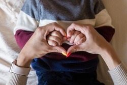 Heart shape created from young woman fingers. Infant hands on mother arms. Lovely emotional, sentimental moment. Closeup. Point of view shot.