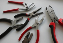 Variety types of pliers with rubberized handles laid out on a white surface