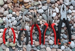 Slip Joint Pliers, Groove Pliers, Needle Nose Pliers And Linesman Pliers Laid Out Arranged On Size On A Stones Background
