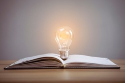 Education knowledge and business studying concept, Closeup glowing light bulb and book on table background.