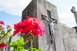 Stone cross with Jesus on a cemetery grave and faded red flowers in front