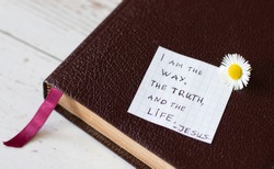 I am the Way, the Truth, and the Life. Jesus Christ's quote in the gospel of John. Handwritten text note on Holy Bible on a wooden background. Christianity concept of faith and hope.