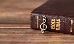 Closed Holy Bible Book with rustic old treble clef note on wooden background. God Jesus Christ is My Song and Salvation. Christian biblical concept of praise, worship, joy in the LORD. A close-up.