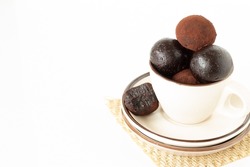 Cup of coffee full of raw chocolate date energy balls coated in cacao powder on a white background with copy space. Healthy homemade vegan dessert or snack.