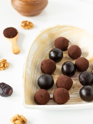 Vegan date walnut energy balls coated in cocoa powder on a rustic heart-shaped plate on white background. Homemade raw chocolate truffles for dessert or snack. Selective focus.