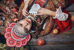 The girl in the red headdress and Russian folk style among apples on dark wooden background top view
