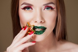 Bright eye makeup and green lips in rhinestones. Unusual look with bright red arrow on her eyes and with a gold star . Close up