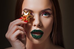 Bright eye makeup and green lips in rhinestones. Unusual look with bright red arrow on her eyes and with a gold star . Close up