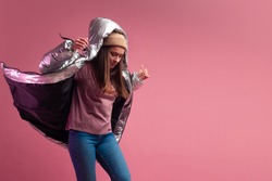 Trendy autumn and winter clothing, Studio shot on a pink background, copy space. A cool woman in a shiny silver down jacket and a knitted hat