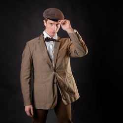 An intelligent gentleman in the Victorian style. Vintage retro suit, young attractive man in a vest and bow tie, he adjusts the cap on his head
