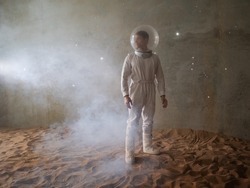 An astronaut on a desert planet alone, an explorer on a distant planet, other worlds and civilizations. A young man in a retrofuturism-style white spacesuit stands on the sand and looks around