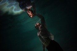 underwater shooting with contrasting light, a guy is swimming underwater, pulling his hand to his reflection in the surface of the water. Subconsciousness and self-reflection, concept