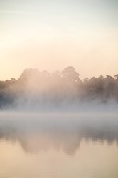 A mist drifts over the pond as the sun gradually lights the sky, the scene offering a moment of serenity and reflection.