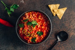 Chili Con Carne in bowl with tortilla chips on dark background. Mexican cuisine. Top view