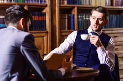 Aristocrats spend leisure in intelligent company. Tea party concept. Oldfashioned intelligent men drink tea according to british tradition. Men in suit sit in library or retro interior, defocused.