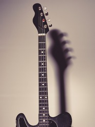 Musical instrument with four strings for playing metal or jazz music. Music and hard rock concept. Guitar in deep black color on black background with shadow. Electric guitar stands on dark chair.