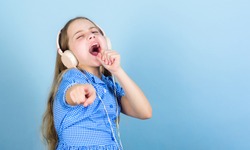 Theres a song for every emotion. Adorable amateur karaoke song singer on blue background. Cute small child doing vocal on song. Little girl singing song playing in headphones, copy space.