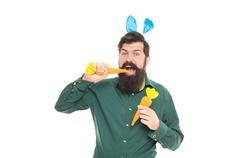 Delicious Easter treats. eastertide. happy bearded man wear bunny ears. happy easter carrot. hipster wearing rabbit ears. time for fun. cheerful guy bite carrots. spring holiday greeting.