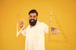 Triangles only have three sides. School teacher or university student smiling with geometric triangles for geometry lesson. Happy hipster holding triangles on yellow background. Lesson in triangles