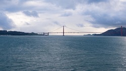 Scenic waterscape with bridge structure over sea water under cloudy sky, golden gate