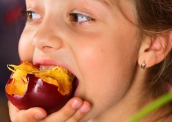 Girl eats fresh, ripe and tasty plum, close up. Kid bites delicious fruit and looks aside. Summer nutrition and healthy food concept