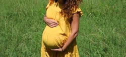 Middle body section of pregnant woman on her third trimester holding and feeling her belly with her hands, against outdoors background.
