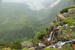 Pancavsky waterfall in czech mountains Krkonose, Giant Mountains. Deep green valley covered with the forest. Rocks above the walley with watrfall. Mountain stream falling from the rocks to the valley.