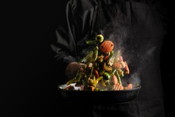Chef cooking vegetables on a pan. Black background for copy text.