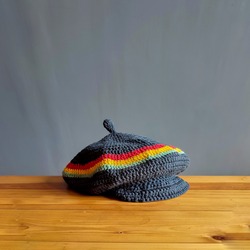 Homemade rasta pattern flat hat with knitting technique with red, yellow and green stripes, placed on a brown wooden table.