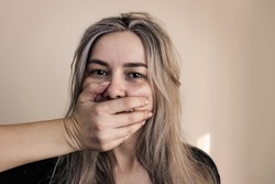 violence against women.domestic violence. young frightened woman covering her mouth with her hand so as not to cry out loud, surprised and amazed, isolated on a dark background in the concept of viole