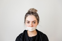 violence against women. domestic violence. young frightened woman, sealed mouth with tape, isolated on dark background.silence,limitation of freedom of speech. in the concept of violence against women