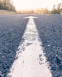 Conceptual image of an asphalt road and a direction arrow, the arrow on the road indicates the direction forward. dawn on the horizon.dawn on the way,