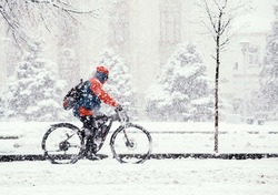 A man in a blue and red jacket rides a bicycle in winter