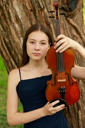 beautiful girl with a violin by the tree in the park. High quality photo