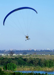 pilot flying motorized paraglider over lake in city park