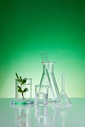 Assorted laboratory glassware equipment showcase with leaves on green backround. Stage showcase cosmetics on glass pedestal modern in laboratory equipment.
