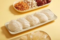 Raw bird's nest is arranged on a long rectangular plate, herbs with cordyceps, lotus seed, jujube and rock sugar are on beige background. Food good for health, increase resistance and anti-aging.
