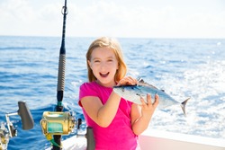 Blond kid girl fishing tuna bonito sarda fish happy with trolling catch on boat deck