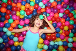little smiling girl playing lying in colorful balls park playground