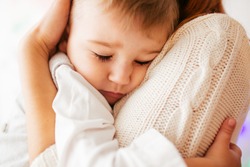 Dreamy little boy hugs his mother tightly sleeping on her shoulder
