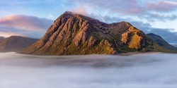 Glencoe, Scotland – September 7, 2019: Colorful, epic panoramic view of mountains at sunrise above a dramatic cloud inversion in Glencoe, Scotland. 