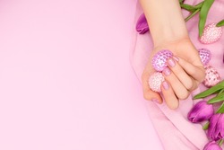 Female hand with glitter purple nail design. Female hand hold easter eggs decorated with purple and pink gems. Model hand with spring nail design on purple background. Copy space.