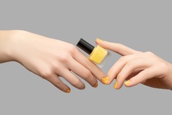 Female hands with yellow nail design. Glitter yellow nail polish manicure with nail art. Woman hands hold yellow nail polish bottle on gray background.