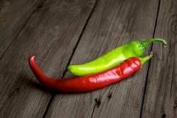 On a wooden table are two pods of hot peppers, red and green. Two pods sharp. Hot peppers of green and red colors on a wooden background.