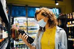 Young woman wearing protective face mask chooses wine in grocery store.