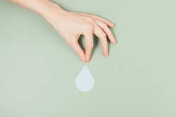Hand holds falling drop on green background. World Water Day, shortage of drinking water, save water concept